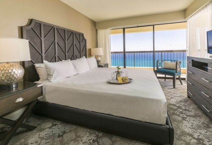 Aston Waikiki Beach Tower gay-friendly hotel room. King bed with ocean view balcony, champagne. Luxury travel for gay men in Waikiki, Hawaii.