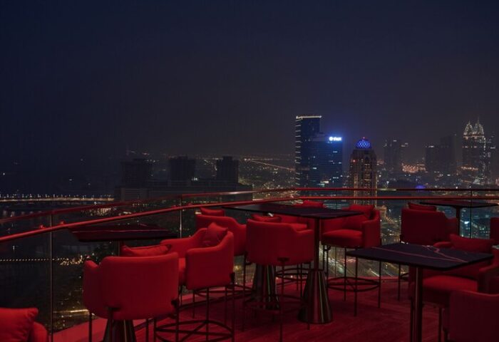 W Dubai - Mina Seyahi gay-friendly hotel rooftop bar at night. Red chairs and tables overlook the Dubai skyline. Gay travel advice.