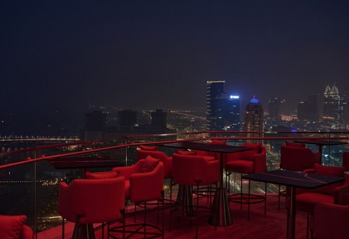 W Dubai - Mina Seyahi gay-friendly hotel rooftop bar at night. Red chairs and tables overlook the Dubai skyline. Gay travel advice.