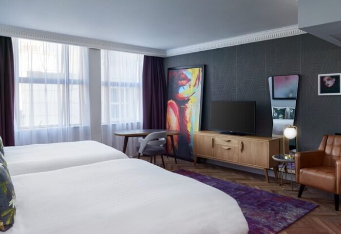 NYX Hotel London Holborn room. Gay-friendly hotel with two beds, TV, modern art, and a stylish brown leather armchair. Comfy stay.