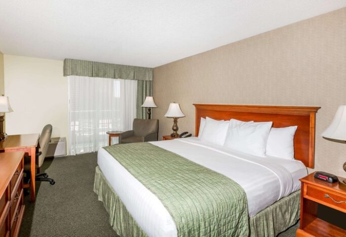 Ramada Plaza by Wyndham Waikiki gay-friendly hotel room. King bed with green accents, desk, chair, and balcony. Comfortable stay in Waikiki.