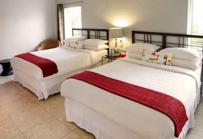 The Cabanas Guesthouse & Spa gay men's resort: Room with two beds, red runner, and decorative pillows. Gay-friendly hotel room interior.