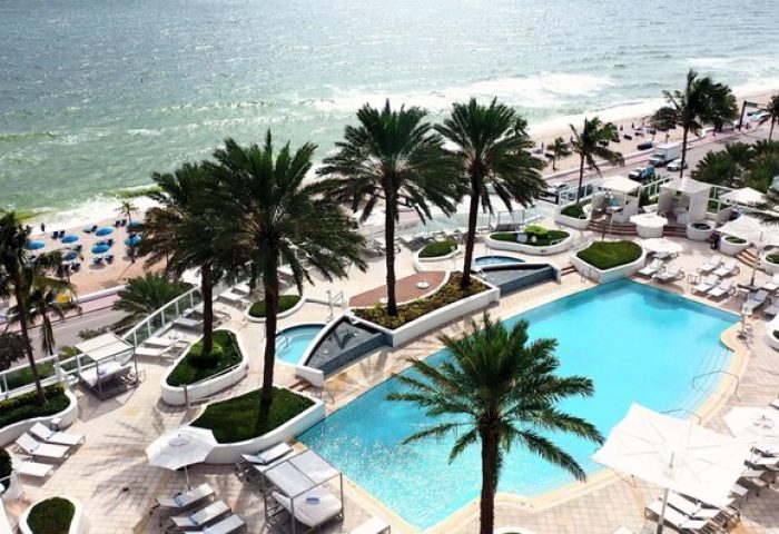 Hilton Fort Lauderdale Beach Resort pool and beach view. Gay-friendly hotel with palm trees, lounge chairs, and ocean access.