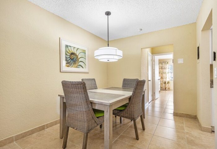 Dining area at Coconut Bay Resort, a gay-friendly hotel. Table with four chairs, modern light fixture, and artwork. Interior of gay hotel room.