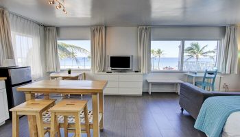 Gay-friendly hotel room with beach view. Interior of a modern apartment featuring a living area, kitchen, and windows overlooking the ocean.
