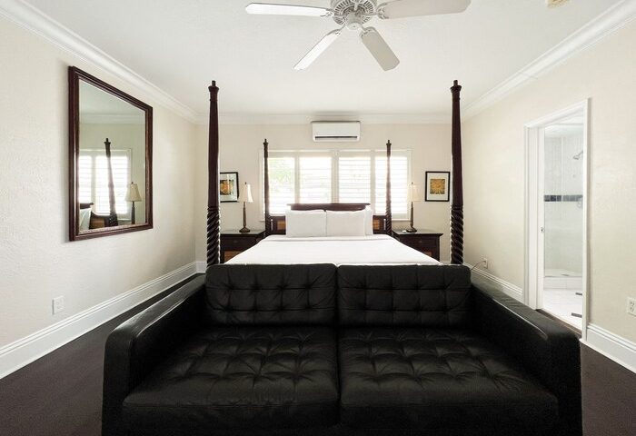 La Casa Hotel room interior. Gay-friendly hotel with a black leather sofa, four-poster bed, ceiling fan, and bathroom. Travel advice.