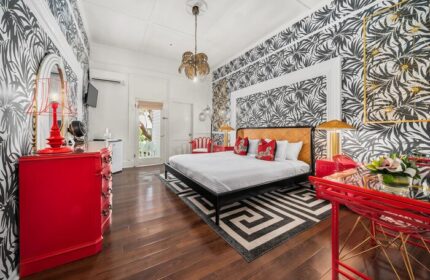 Marrero's Guest Mansion gay-friendly hotel room. Red accents, patterned wallpaper, king bed, and stylish decor for gay men's travel.