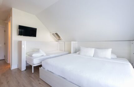 NYAH Key West adults-only, gay-friendly hotel room. Clean, white interior with a king bed, a twin bed, and a flat-screen TV.
