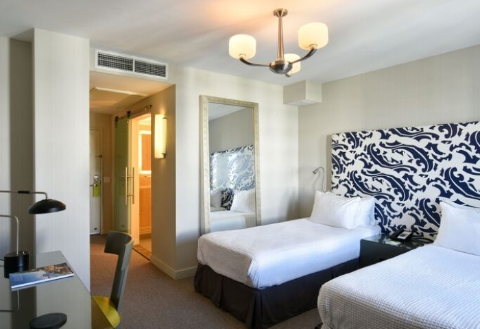 Hotel Breakwater South Beach gay-friendly room. Twin beds with patterned headboard, desk, and bathroom. Modern design for gay travelers.