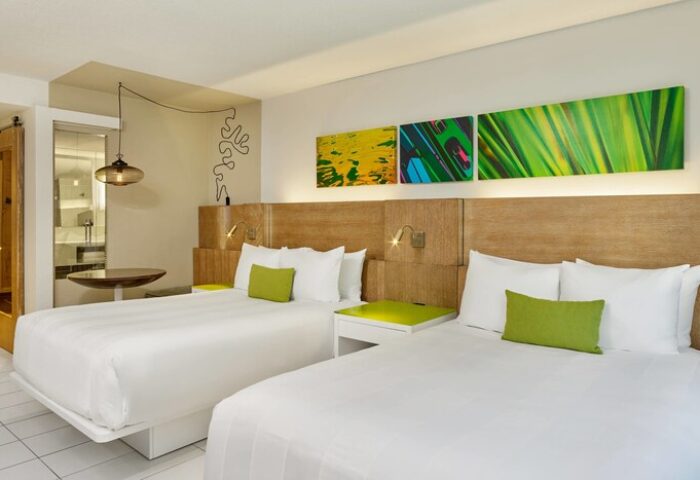 Royal Palm South Beach Miami gay-friendly hotel room. Two beds with white linens, green accents, and modern art. Bathroom visible.