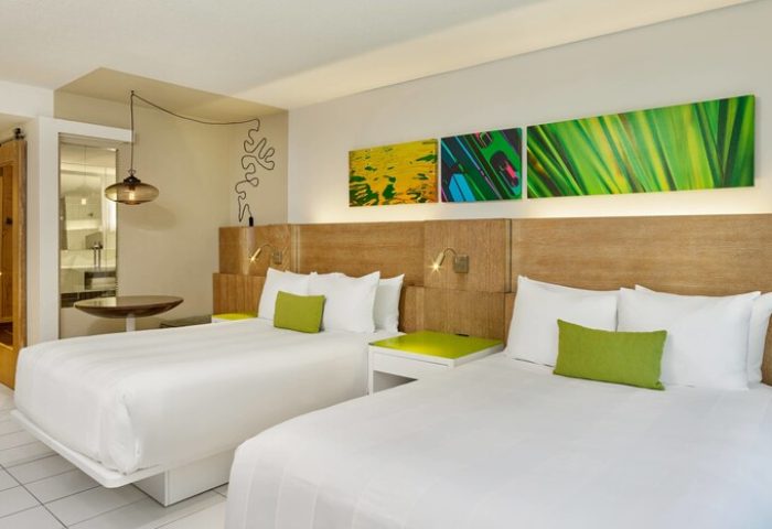 Royal Palm South Beach Miami gay-friendly hotel room. Two beds with white linens, green accents, and modern art. Bathroom visible.