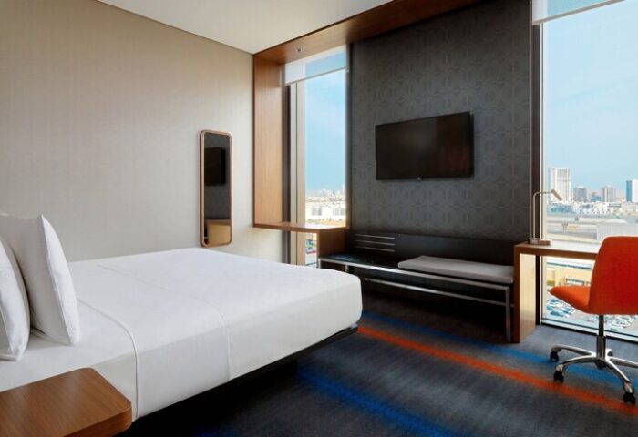 Aloft Me'aisam Dubai hotel room. Gay-friendly hotel with bed, desk, TV, and city view. Modern design, comfortable for gay travelers.