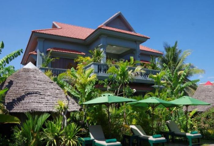 3 Monkeys Villa gay hotel. Exterior view of a gay-friendly, pet-friendly hotel with tropical foliage, lounge chairs, and thatched huts.