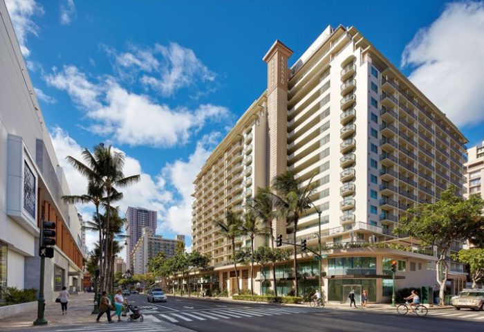 Hilton Garden Inn Waikiki Beach exterior. Gay-friendly hotel with palm trees, balconies, and a crosswalk. Waikiki travel for gay men.