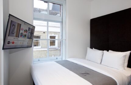The Z Hotel Covent Garden room. Gay-friendly hotel with TV, window view, bed, and gray throw. Modern, compact design for gay travelers in London.