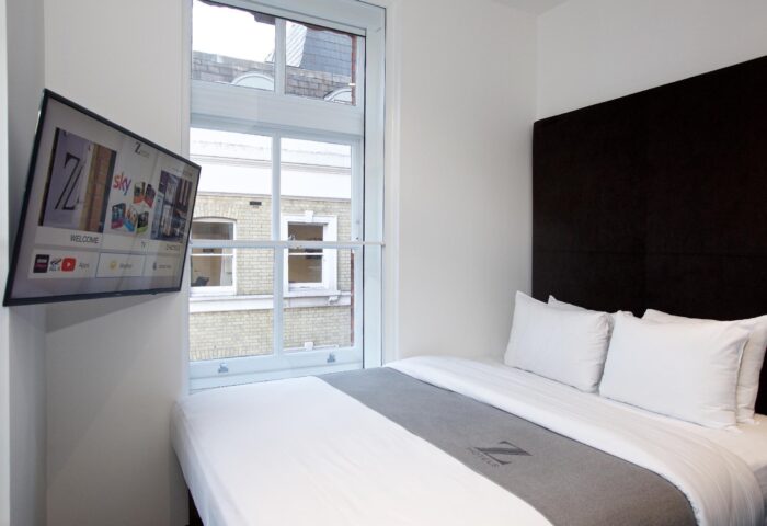 The Z Hotel Covent Garden room. Gay-friendly hotel with TV, window view, bed, and gray throw. Modern, compact design for gay travelers in London.