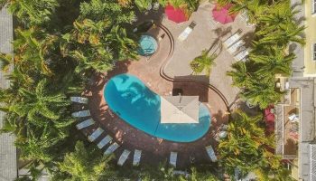 Aerial view of The Grand Resort and Spa, an all-male, gay-friendly hotel. Pool, jacuzzi, lounge chairs, and palm trees visible.