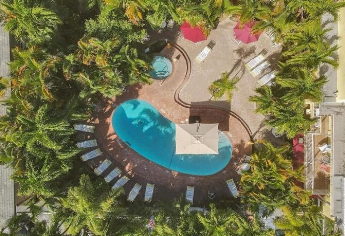 Aerial view of The Grand Resort and Spa, an all-male, gay-friendly hotel. Pool, jacuzzi, lounge chairs, and palm trees visible.