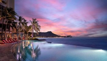 Sunset at Sheraton Waikiki Beach Resort, a gay-friendly hotel. Infinity pool, Diamond Head view, palm trees, and cabanas. Waikiki gay travel.