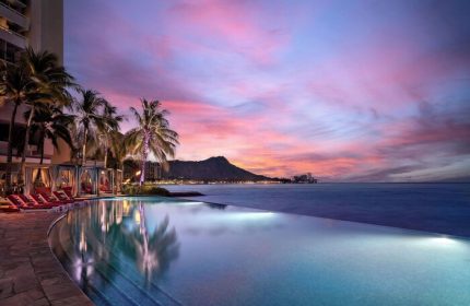 Sunset at Sheraton Waikiki Beach Resort, a gay-friendly hotel. Infinity pool, Diamond Head view, palm trees, and cabanas. Waikiki gay travel.