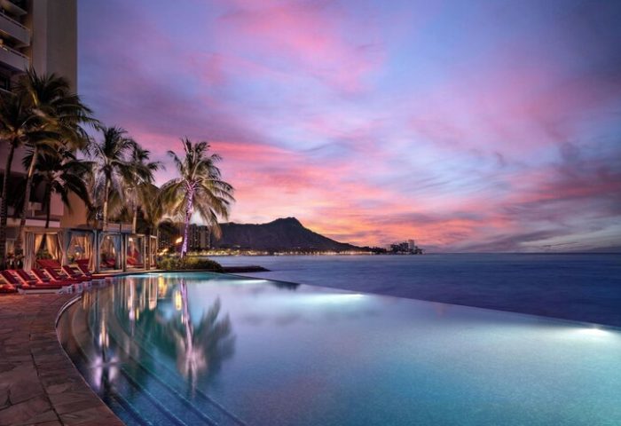 Sunset at Sheraton Waikiki Beach Resort, a gay-friendly hotel. Infinity pool, Diamond Head view, palm trees, and cabanas. Waikiki gay travel.