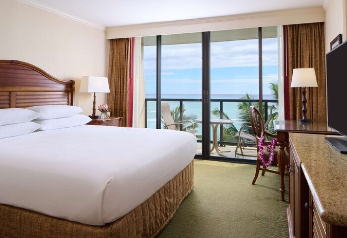 OUTRIGGER Waikiki Beach Resort gay-friendly hotel room. Ocean view from balcony. King bed, desk, TV, and chair with lei. Hawaii travel.