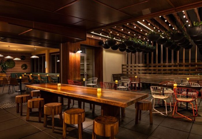 The Laylow, Autograph Collection gay-friendly hotel outdoor dining. Long wooden table with stools, string lights, and hanging plants create a warm ambiance.