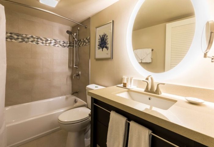 Bathroom at Aston Waikiki Beach Tower, a gay-friendly hotel. Bathtub, toilet, and sink with illuminated mirror. Ideal for gay men's travel.