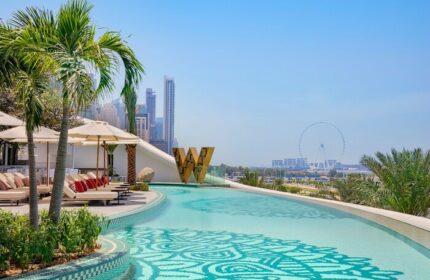 W Dubai - Mina Seyahi gay-friendly hotel pool view. Palm trees, lounge chairs, and Dubai skyline. A luxurious travel destination for gay men.