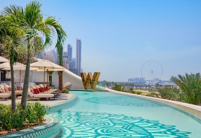 W Dubai - Mina Seyahi gay-friendly hotel pool view. Palm trees, lounge chairs, and Dubai skyline. A luxurious travel destination for gay men.