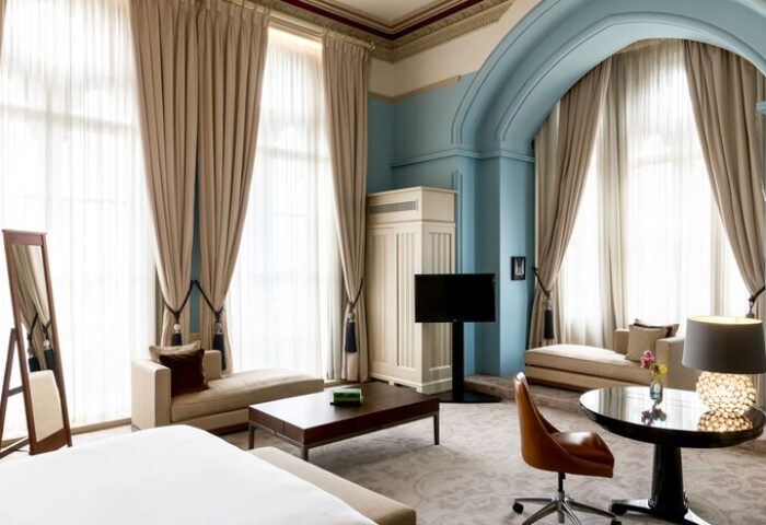 St. Pancras Renaissance Hotel London room. Gay-friendly hotel with luxury interior, large windows, chaise lounges, and a modern TV.
