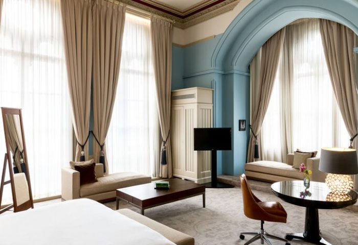 St. Pancras Renaissance Hotel London room. Gay-friendly hotel with luxury interior, large windows, chaise lounges, and a modern TV.