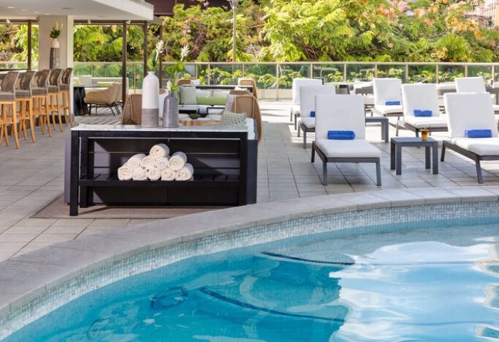 Hilton Garden Inn Waikiki Beach gay-friendly hotel pool area. Lounge chairs, towels, and bar seating. Ideal for gay men travel in Honolulu.