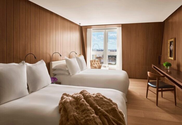 The London EDITION hotel room with two beds, wood paneling, desk, and London Eye view. Gay-friendly hotel for gay men travel advice.