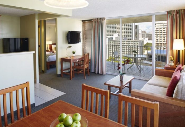 Pacific Monarch Hotel gay-friendly suite. Living area, dining table with apples, balcony with city view. Ideal for gay travel.