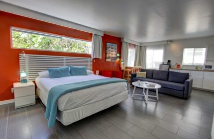 Gay-friendly hotel room with bed, seating area, and kitchenette. Modern design, orange accent wall. Ideal for gay men's travel. Snooze in style.