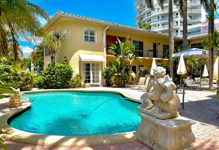 La Casa Hotel, a gay-friendly hotel, features a pool, statue, palm trees, and lounge chairs, ideal for gay men's travel and relaxation.