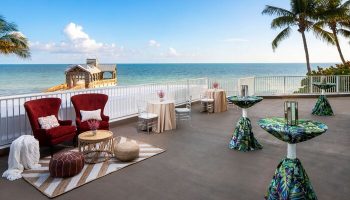 The Reach Key West, Curio Collection by Hilton, a gay-friendly hotel. Ocean view from the terrace with tables and chairs. Pier in the background.