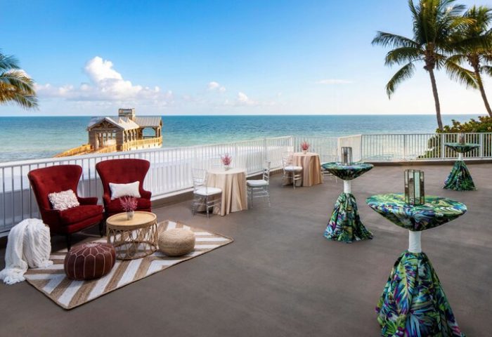 The Reach Key West, Curio Collection by Hilton, a gay-friendly hotel. Ocean view from the terrace with tables and chairs. Pier in the background.