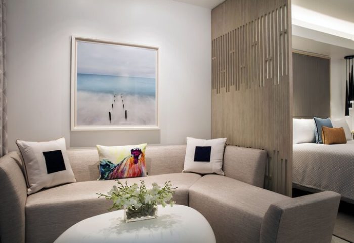 H2O Suites Adults Only gay-friendly hotel room. Modern design with a sectional sofa, ocean art, and partial view of the bed. Stylish, upscale.