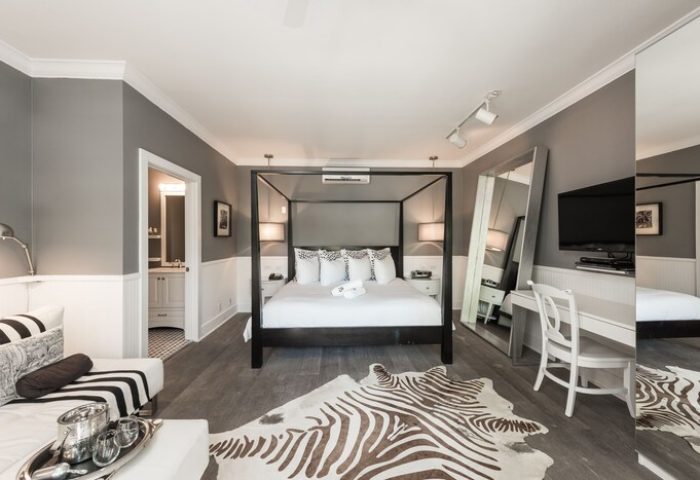 Gay-Friendly Hotel room at Alexander's Guesthouse. Features a four-poster bed, zebra rug, desk, and modern decor. Stylish gay travel lodging.