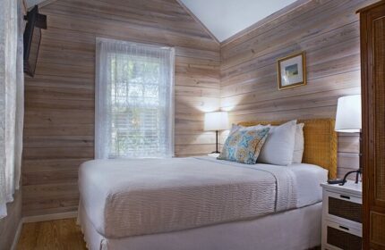 Island City House gay-friendly hotel room. Cozy bedroom with white bedding, wood-paneled walls, and natural light. A comfortable stay for gay travelers.