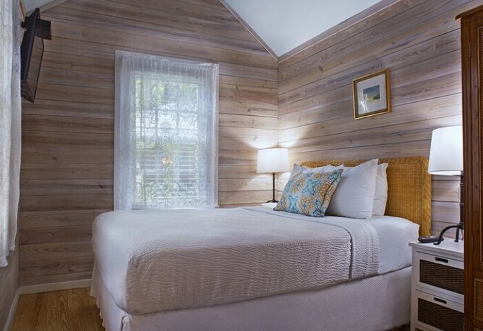 Island City House gay-friendly hotel room. Cozy bedroom with white bedding, wood-paneled walls, and natural light. A comfortable stay for gay travelers.