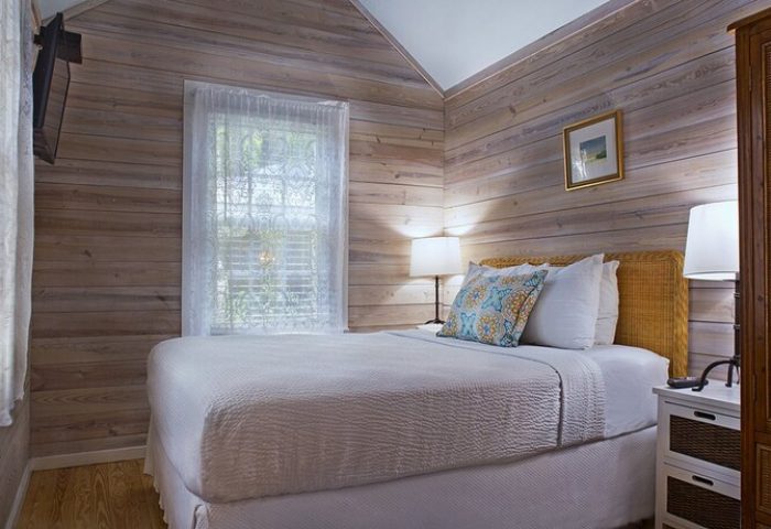 Island City House gay-friendly hotel room. Cozy bedroom with white bedding, wood-paneled walls, and natural light. A comfortable stay for gay travelers.