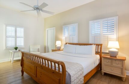 Paradise Inn adults-only gay-friendly hotel room. Bedroom with wood bed frame, white linens, ceiling fan, and shuttered windows.