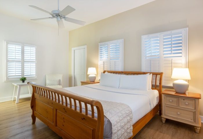 Paradise Inn adults-only gay-friendly hotel room. Bedroom with wood bed frame, white linens, ceiling fan, and shuttered windows.