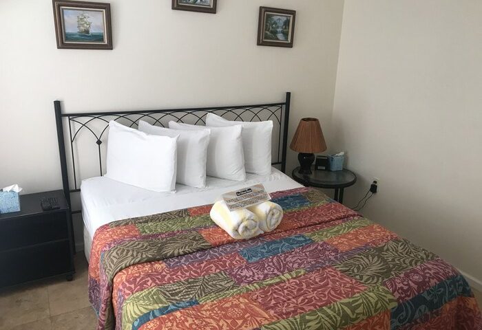 Bedroom at gay-friendly New Orleans House. Bed with colorful quilt, white pillows, & wrought iron headboard. Nightstands on each side.