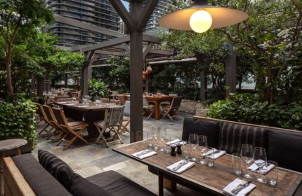 EAST Miami gay-friendly hotel outdoor dining area. Tables are set with glasses and silverware. Lush greenery surrounds the patio.