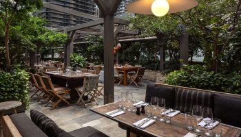 EAST Miami gay-friendly hotel outdoor dining area. Tables are set with glasses and silverware. Lush greenery surrounds the patio.