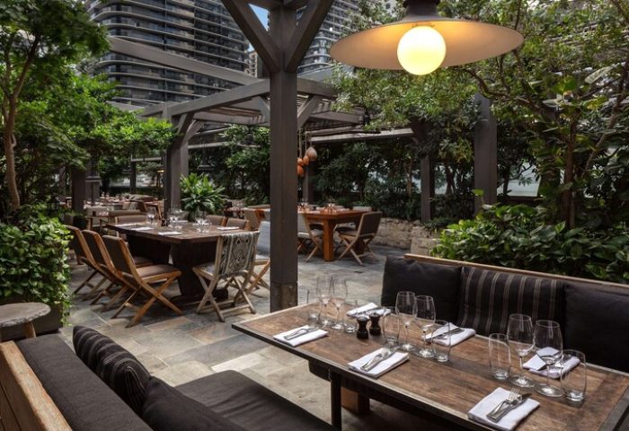 EAST Miami gay-friendly hotel outdoor dining area. Tables are set with glasses and silverware. Lush greenery surrounds the patio.